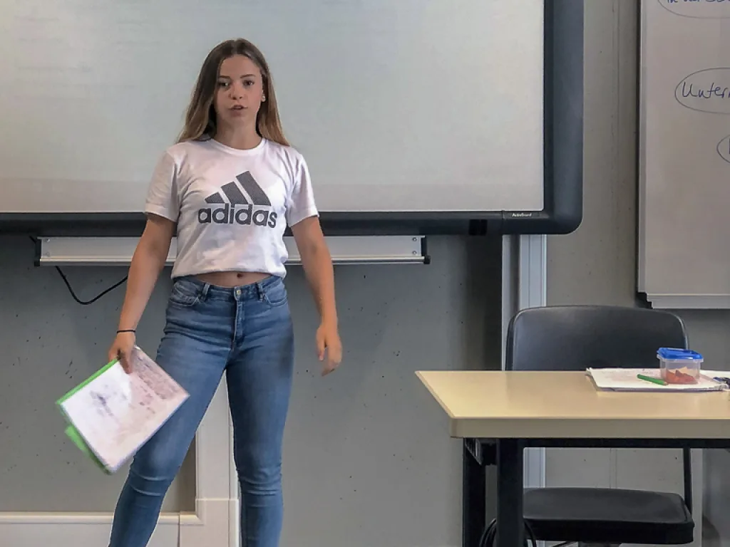 Jugendliche steht mit einem Blatt vor der Klasse.